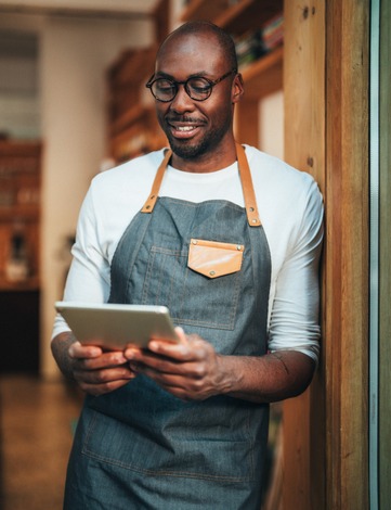 Smiling person in apron holding tablet in shop
